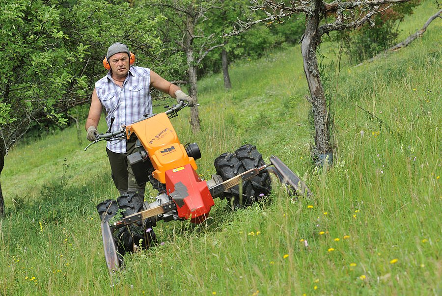 Ein Mann mäht einen steilen Hang mit einer Maschine.
