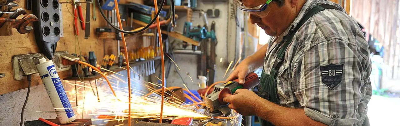 Ein Mann arbeitet mit einer Flex an einer Werkbank.