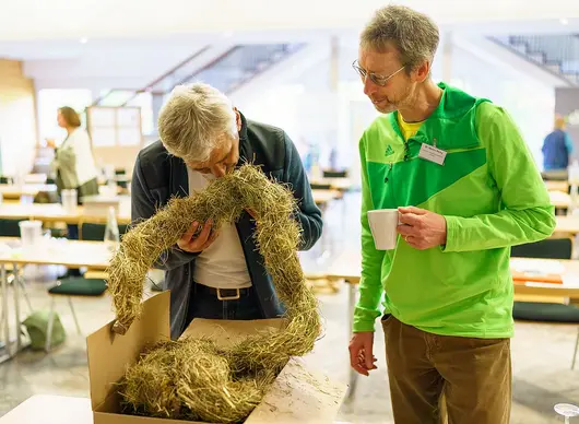 Zwei Männer schauen sich einen Heustrang genauer an.