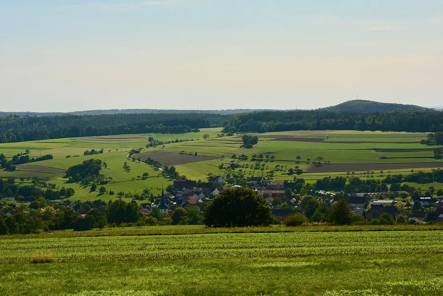 Wiese mit Ortschaft und hügelige Waldlandschaft
