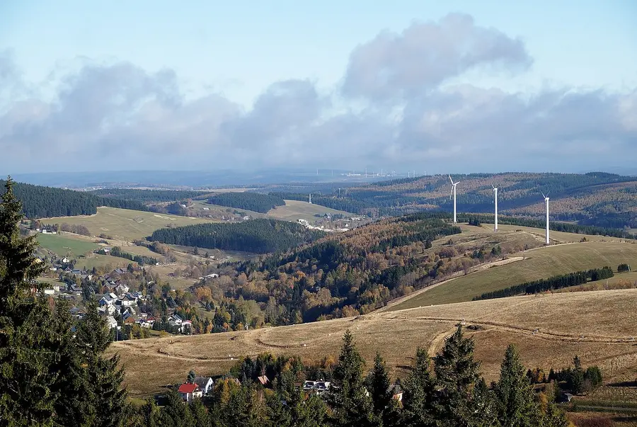 hügelige Landschaft mit Wiesen, Windrad und Ortschaft